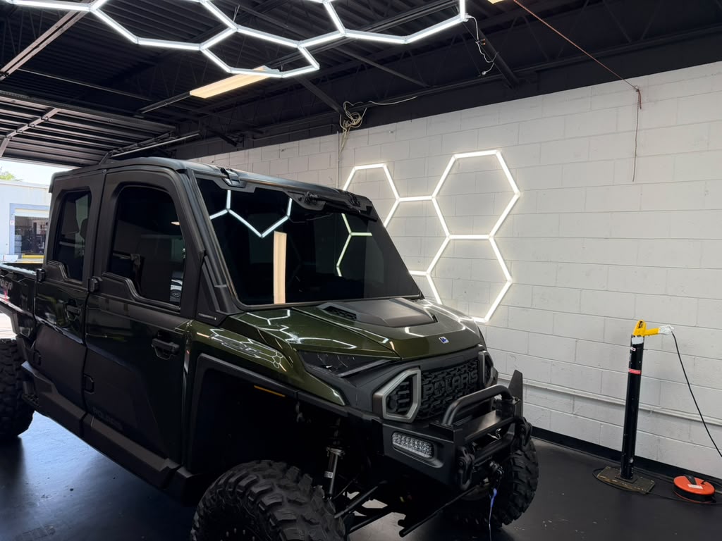 Green Polaris-style UTV with dark tinted windows under hex lighting