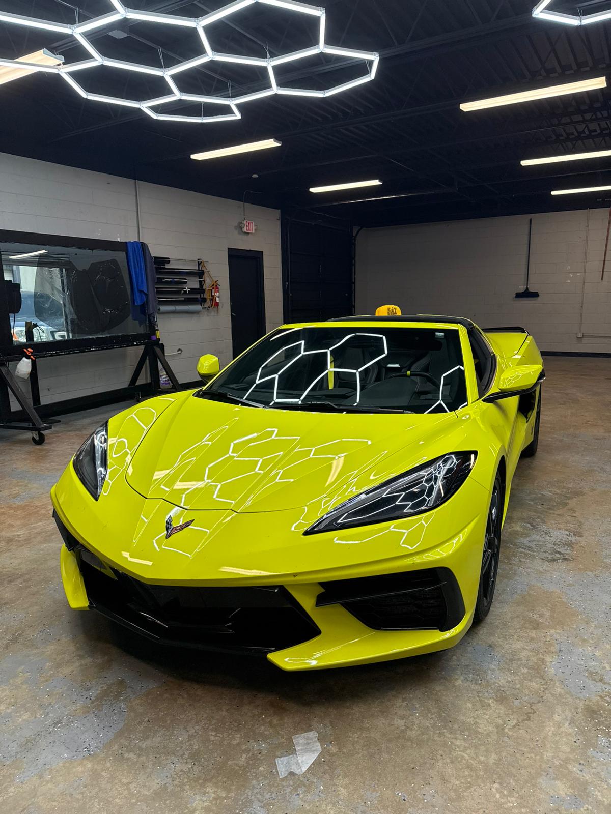 Bright yellow Corvette with fresh window tint under hexagonal shop lights